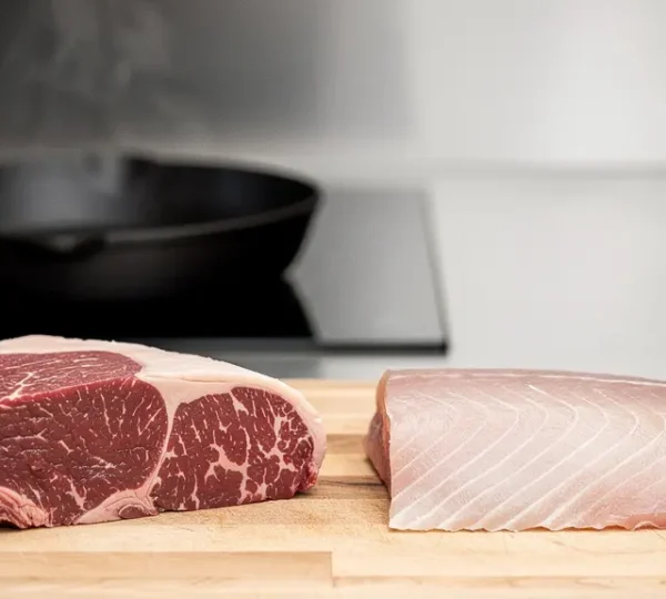 Plan large editorial de morceaux de viande et de poisson sur un plan de travail, avec vapeur et zones vides pour illustrer l'effet de la chaleur sur les proteines.